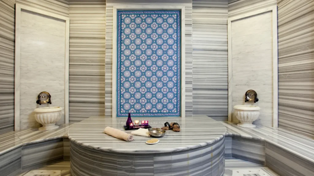 Therapist performing kese scrub on marble platform.